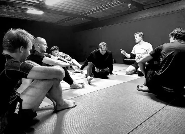 Uitleg op de mat: de groep luistert naar de trainer